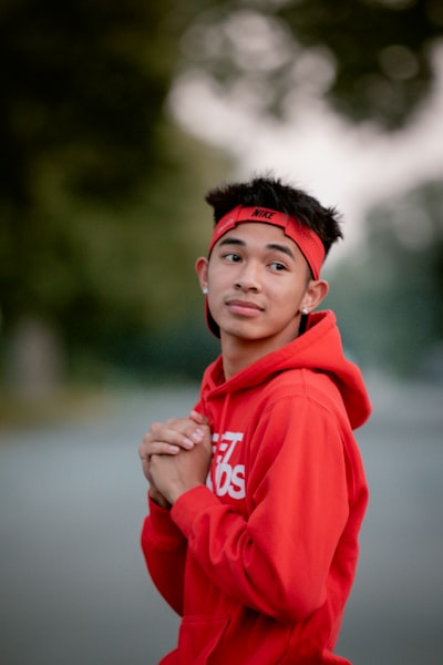 A young man in an orange hoodie is posing for a picture