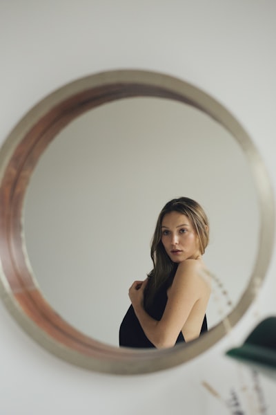 Woman in black sleeveless dress sitting on round mirror