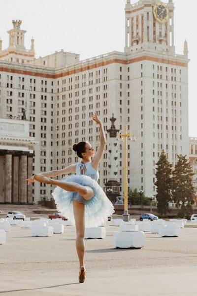 Ballerina dancing near white concrete building during daytime