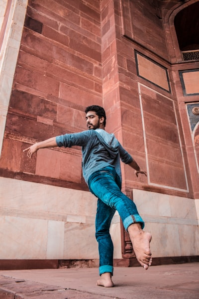 Man in blue denim jeans jumping on brown concrete wall during daytime