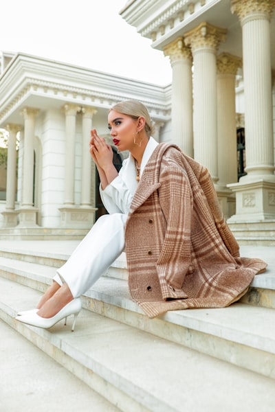 Woman in white pants and red and white plaid coat sitting on white concrete bench