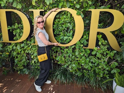 Woman posing by Dior sign in green hedge