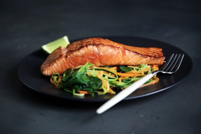 Grilled fish, cooked vegetables, and fork on plate