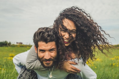Woman riding on man's back on green field