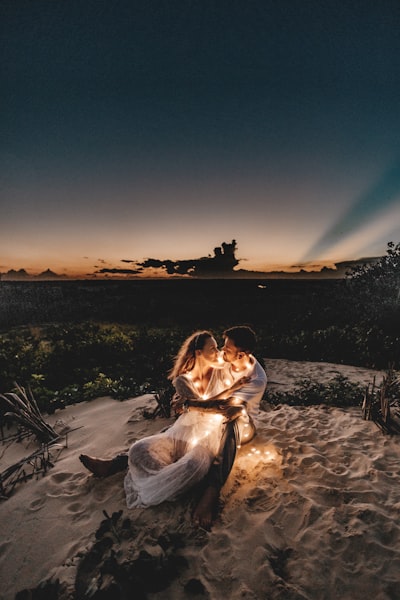 Man and woman looking each other sitting on white sand during sunset