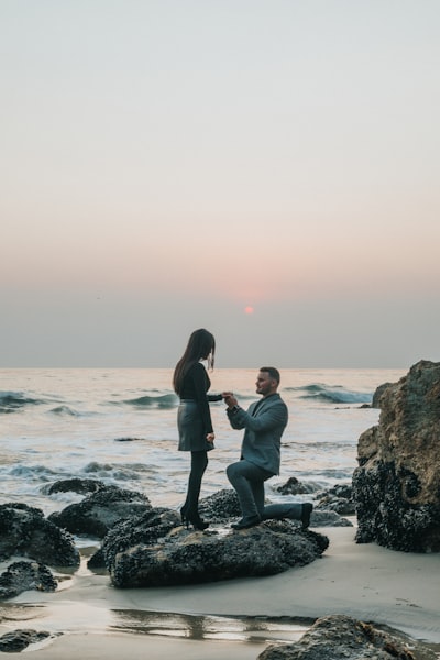Man kneeling in front of woman on rock at beach