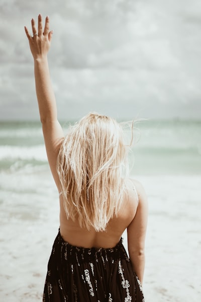 Woman with raised arm facing the ocean on beach