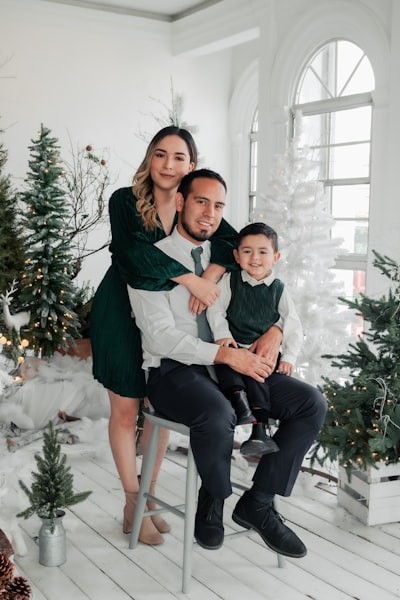 A man, woman and child sitting on a chair in front of a christmas tree