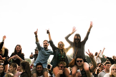 Three men carrying women surrounded by many people during daytime