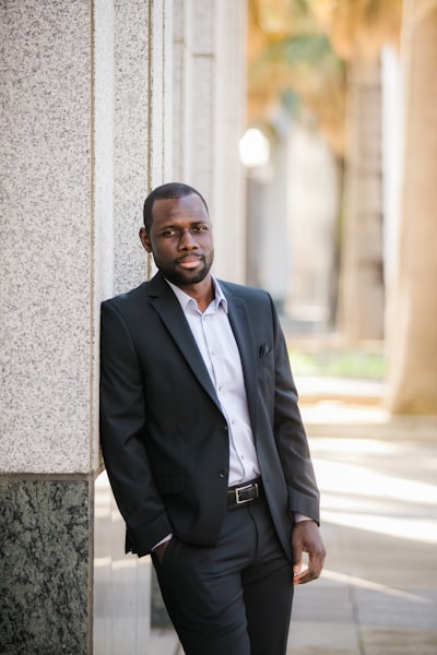 Fortune Vieyra wearing black business suit while standing next to a wall.