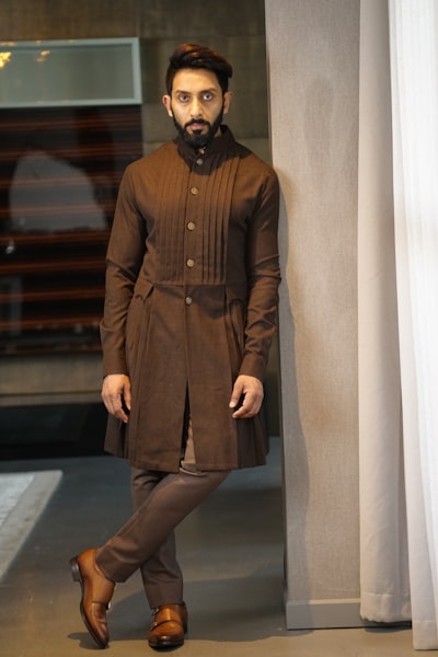 Man in brown pleated kurta leaning against pillar
