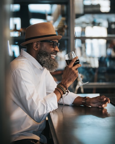 Man in white dress shirt and brown hat holding clear drinking glass