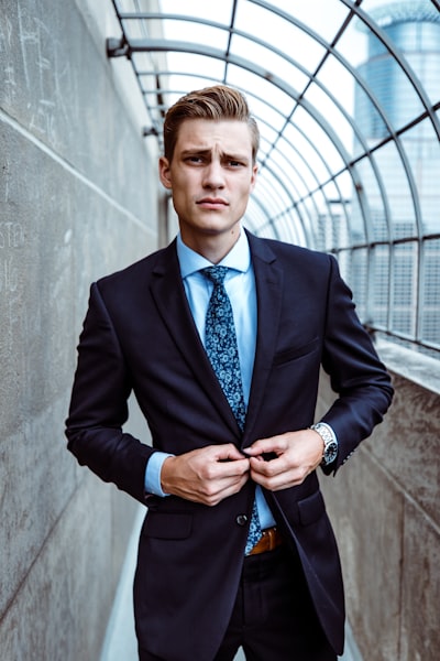 Young man buttoning navy suit in glass walkway