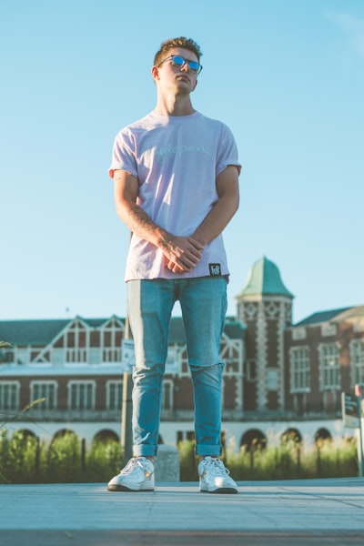Man in white crew neck t-shirt and blue denim jeans standing on green grass field