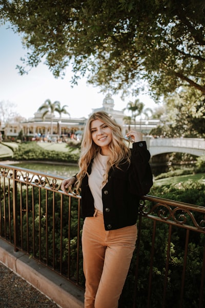 Woman in black jacket and brown pants standing on bridge during daytime