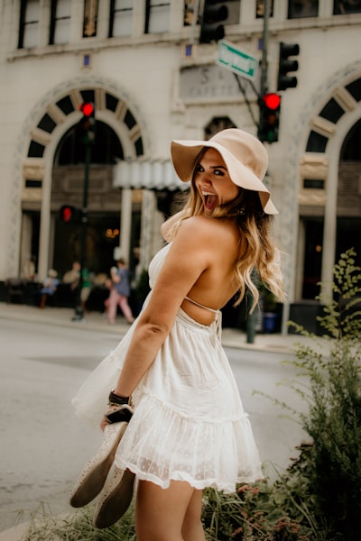 Woman in white spaghetti strap dress wearing white hat standing on road during daytime